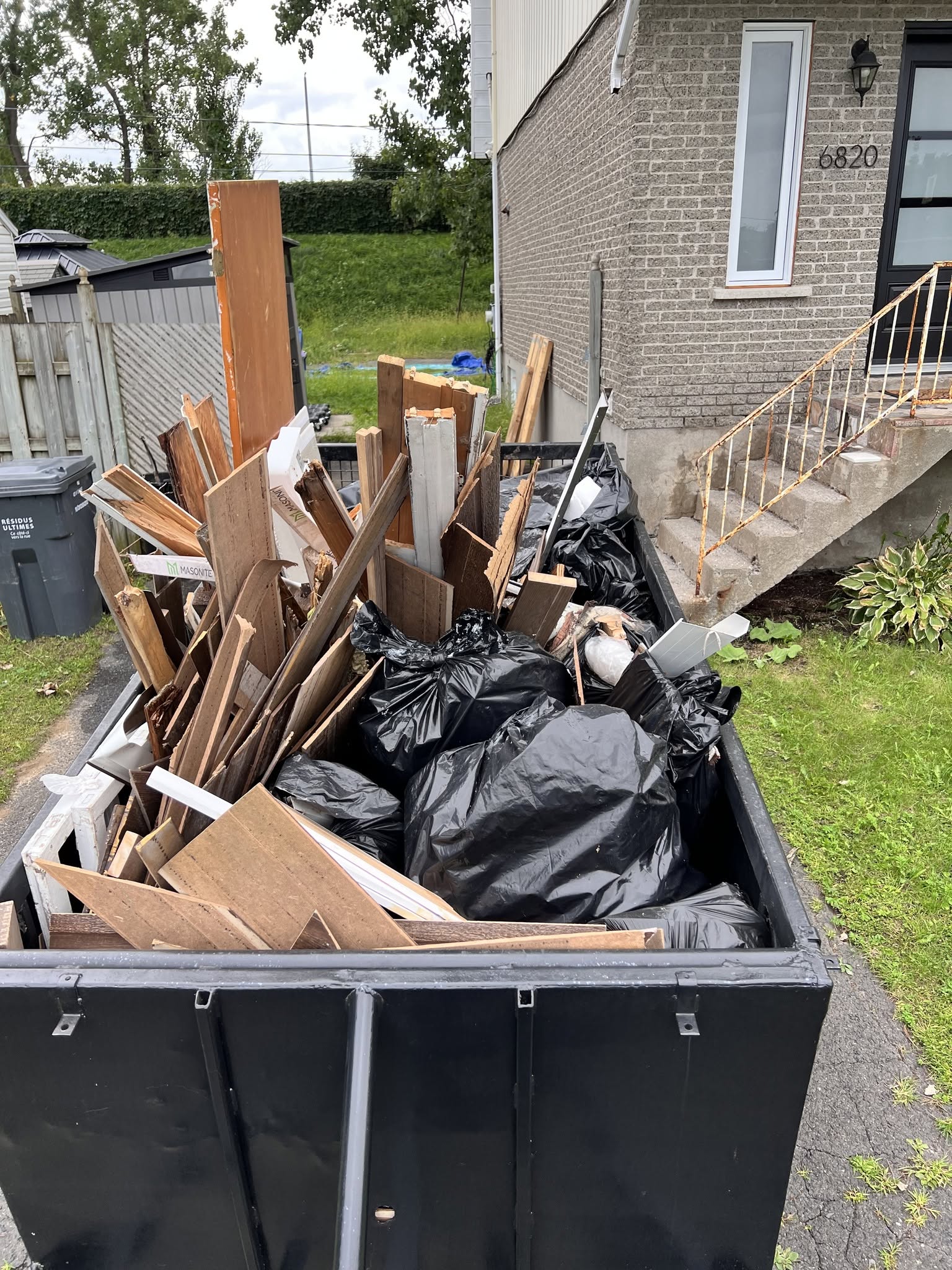 Remorque remplie de planches et de sacs de débris devant une maison