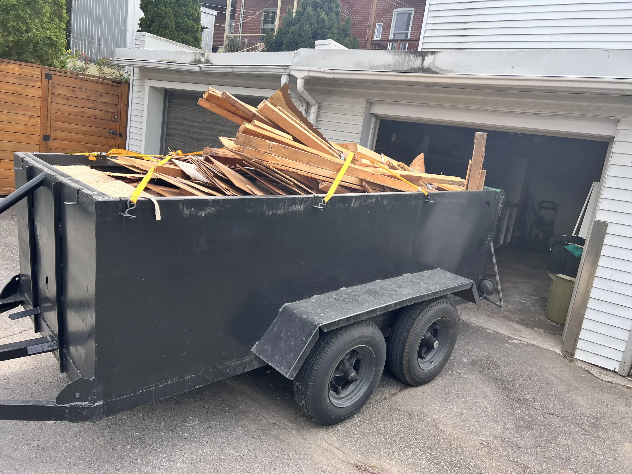 Remorque 5 × 11 chargée de bois de démolition, sanglée, devant un garage